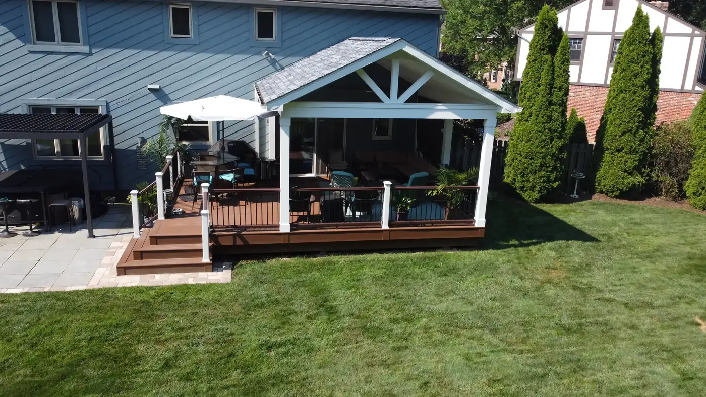 Covered composite deck with a gable roof and wide steps down to a paver patio