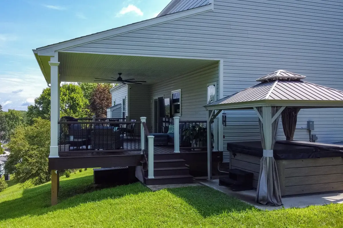 Covered deck with a ceiling fan and black railing next to a hot tub gazebo